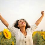 Joyful woman with arms raised in a sunflower field, embracing freedom and happiness.