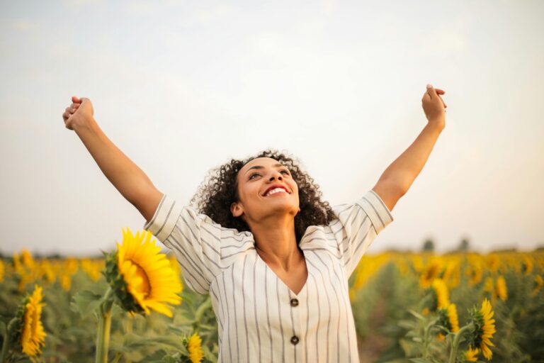 Joyful woman with arms raised in a sunflower field, embracing freedom and happiness.